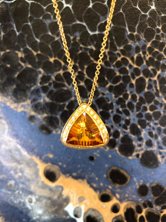 Photo of 18K Gold Citrine Triangle Pendant with Diamond Halo in a decorative scene, designed by , available at Plumb Gold & Plumb Silver