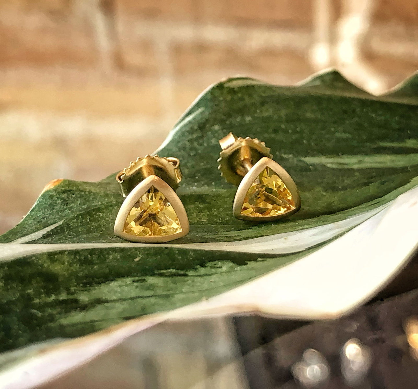 Photo of 18K Yellow Beryl Triangle Bezel Set Stud Earrings in a decorative scene, designed by , available at Plumb Gold & Plumb Silver