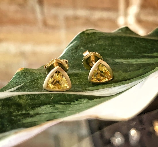 Photo of 18K Yellow Beryl Triangle Bezel Set Stud Earrings in a decorative scene, designed by , available at Plumb Gold & Plumb Silver