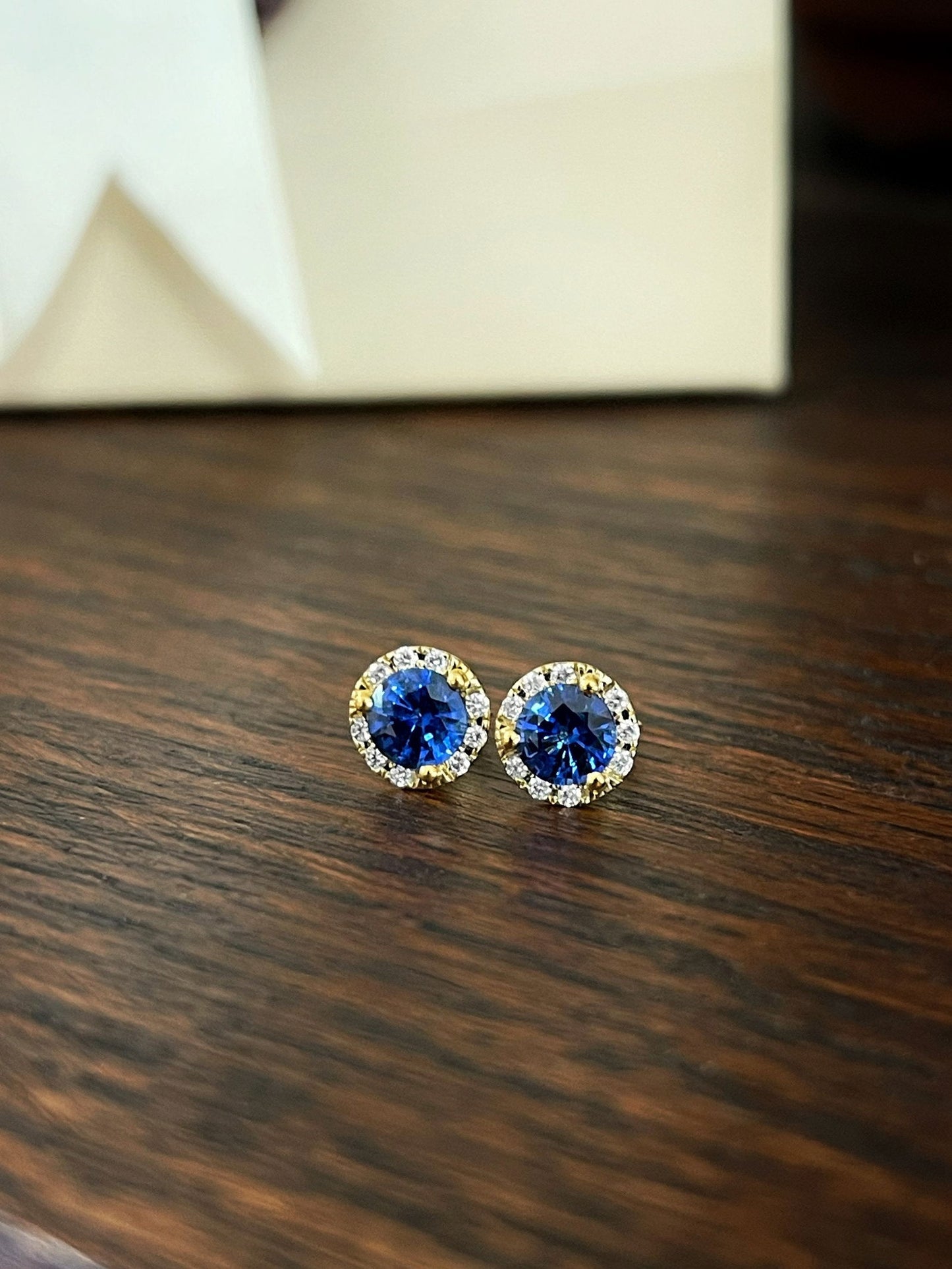 Photo of Blue Sapphire and Diamond Halo Studs in a decorative scene, designed by , available at Plumb Gold & Plumb Silver