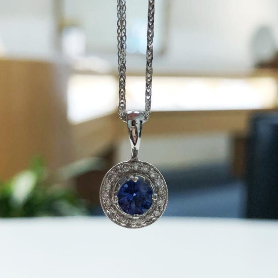 Photo of Blue Sapphire with Diamond Halo Pendant in a decorative scene, designed by , available at Plumb Gold & Plumb Silver