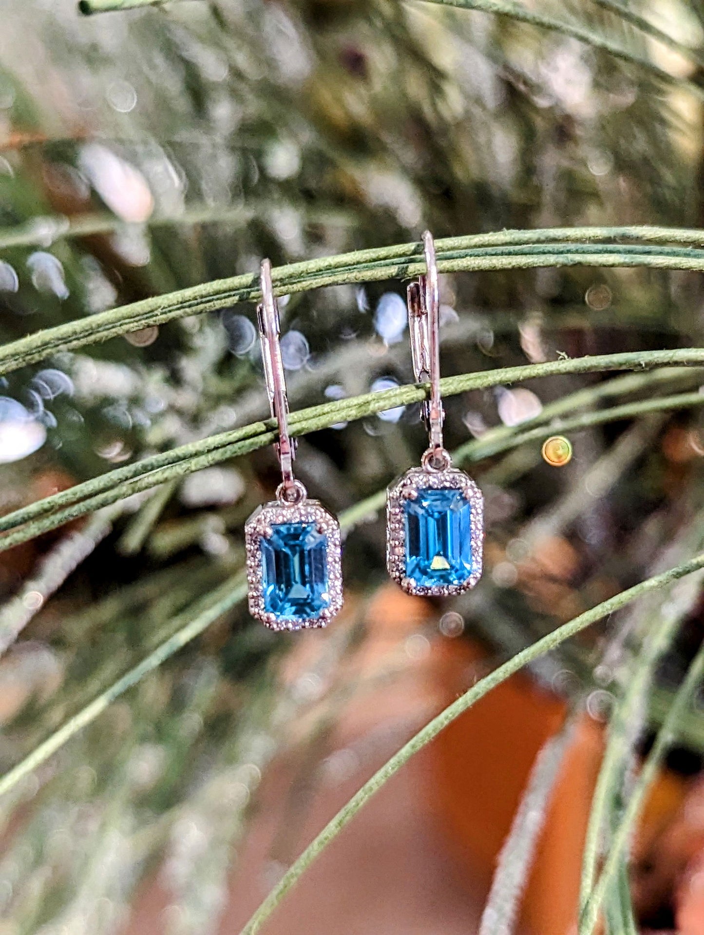 Photo of Blue Zircon Dangle Earrings in a decorative scene, designed by , available at Plumb Gold & Plumb Silver