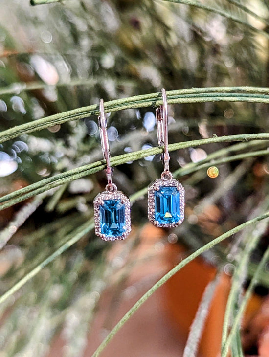 Photo of Blue Zircon Dangle Earrings in a decorative scene, designed by , available at Plumb Gold & Plumb Silver