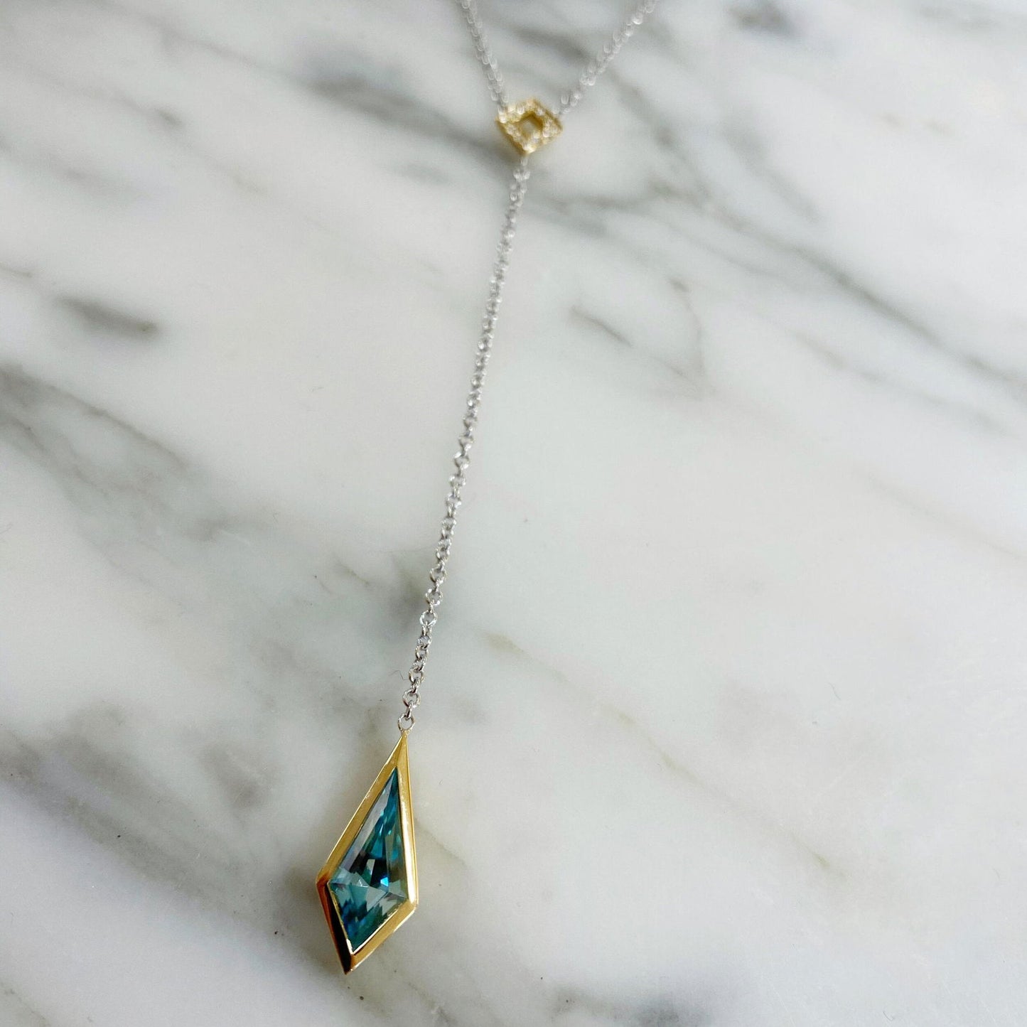 Photo of Blue Zircon Kite "Y" Necklace in a decorative scene, designed by , available at Plumb Gold & Plumb Silver
