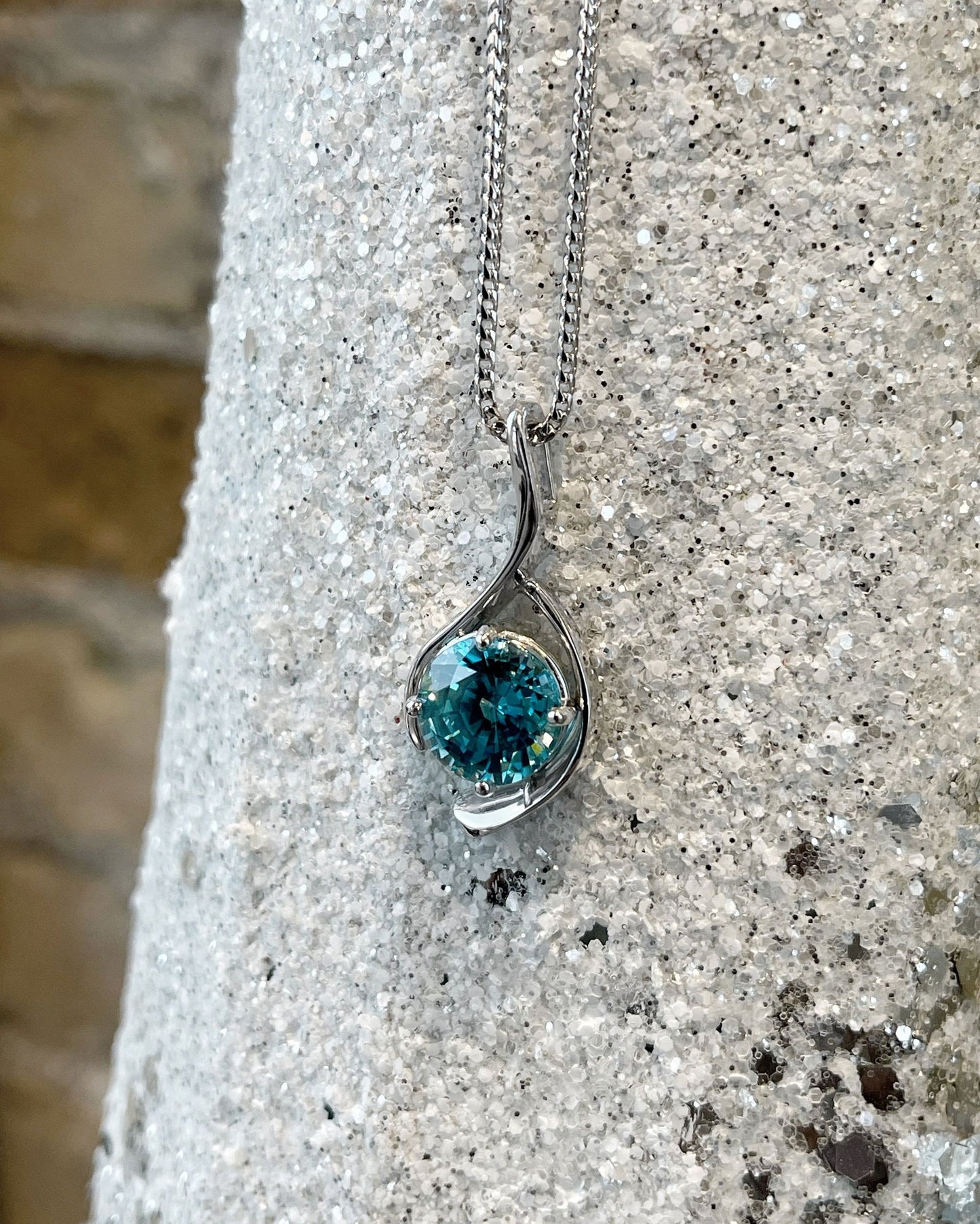 Photo of Blue Zircon Pendant in a decorative scene, designed by , available at Plumb Gold & Plumb Silver