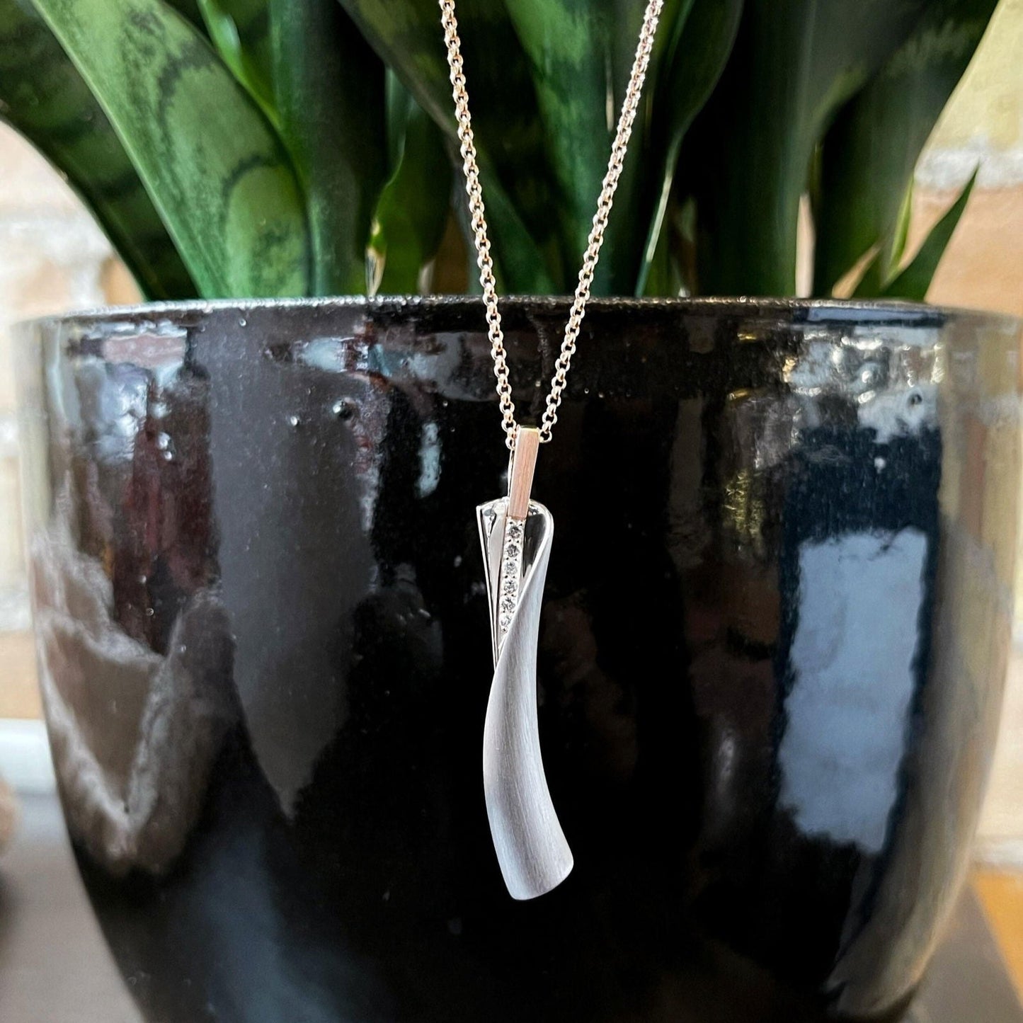 Photo of Breuning White Sapphire Wrap Pendant in a decorative scene, designed by , available at Plumb Gold & Plumb Silver