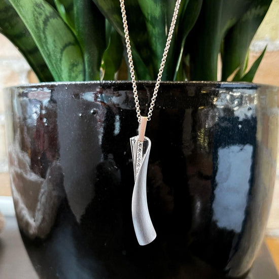 Photo of Breuning White Sapphire Wrap Pendant in a decorative scene, designed by , available at Plumb Gold & Plumb Silver