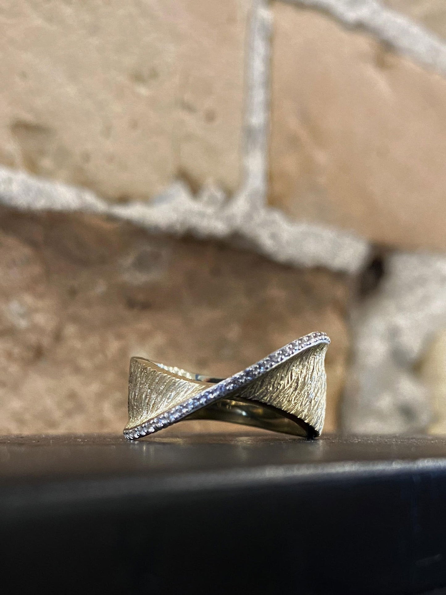Photo of Crossover Ring with White Sapphire Accents in a decorative scene, designed by , available at Plumb Gold & Plumb Silver