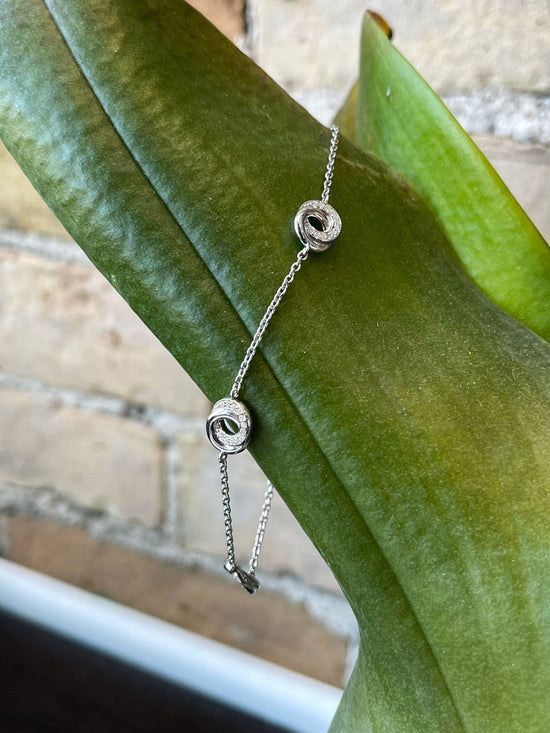 Photo of Cubic Zirconia Entwined Circles Station Bracelet in a decorative scene, designed by , available at Plumb Gold & Plumb Silver