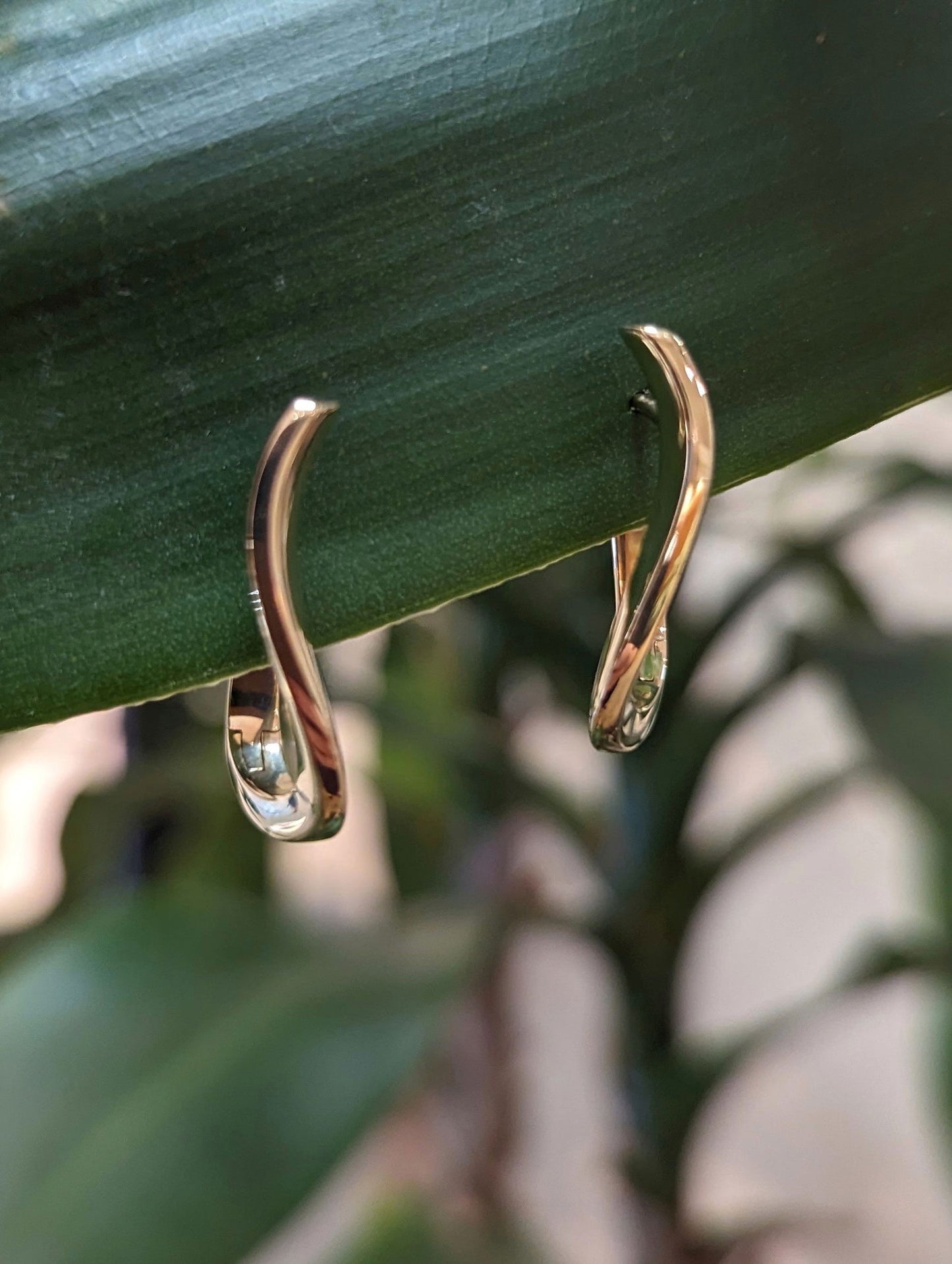 Photo of Curved Huggie Hoop Earrings in a decorative scene, designed by , available at Plumb Gold & Plumb Silver