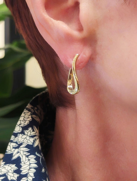 Photo of Curved Huggie Hoop Earrings in a decorative scene, designed by , available at Plumb Gold & Plumb Silver