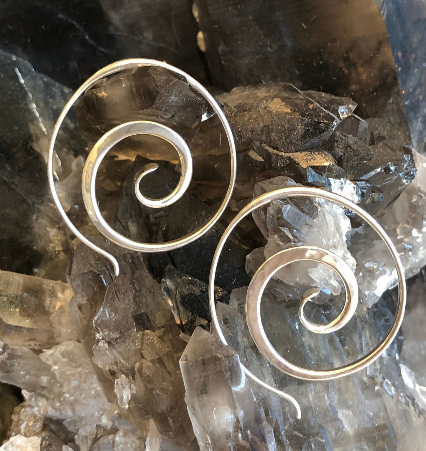 Photo of E L Designs "Crop Circle" Spiral Sterling Silver Hoop Earrings in a decorative scene, designed by , available at Plumb Gold & Plumb Silver