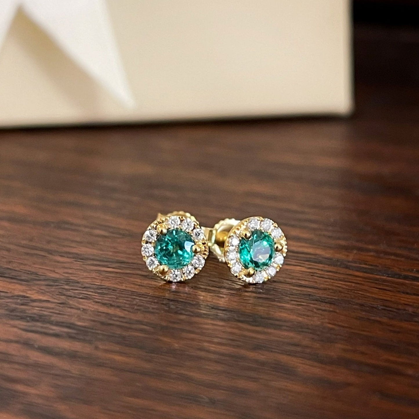 Photo of Emerald and Diamond Halo Studs in a decorative scene, designed by , available at Plumb Gold & Plumb Silver