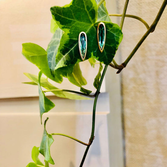 Photo of Green Tourmaline Teardrop Bezel Post Earrings in a decorative scene, designed by , available at Plumb Gold & Plumb Silver
