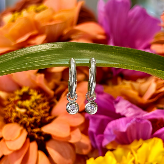 Photo of Huggie Hoops with Diamond Charms in a decorative scene, designed by , available at Plumb Gold & Plumb Silver