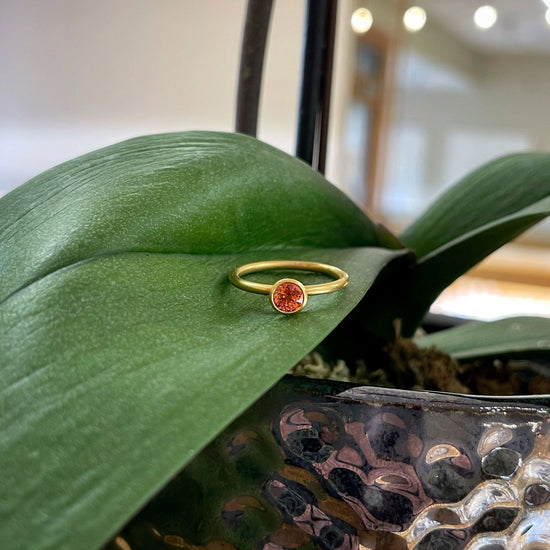 Photo of Kim Collins Orange Sapphire Ring in a decorative scene, designed by , available at Plumb Gold & Plumb Silver