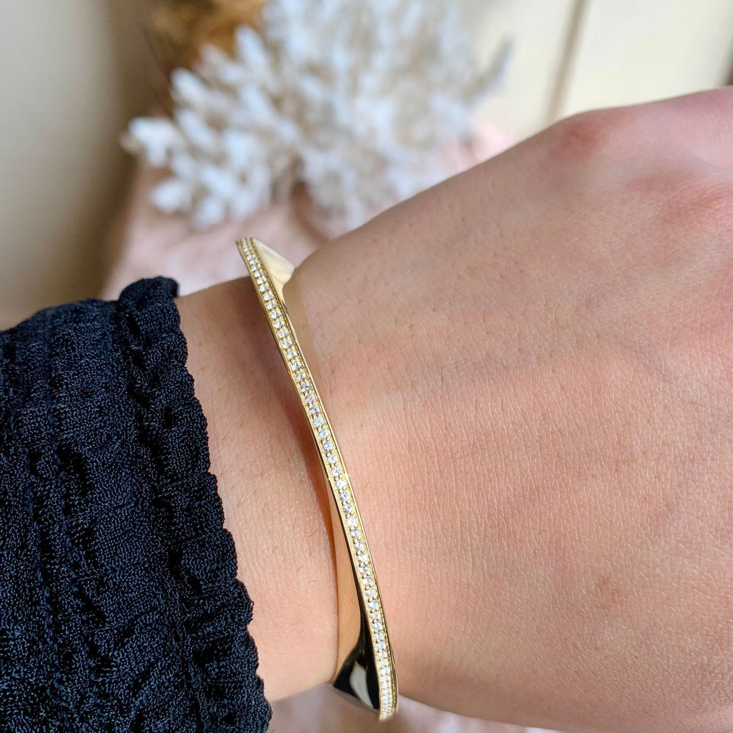 Photo of Mobius White Sapphire Bangle in a decorative scene, designed by , available at Plumb Gold & Plumb Silver