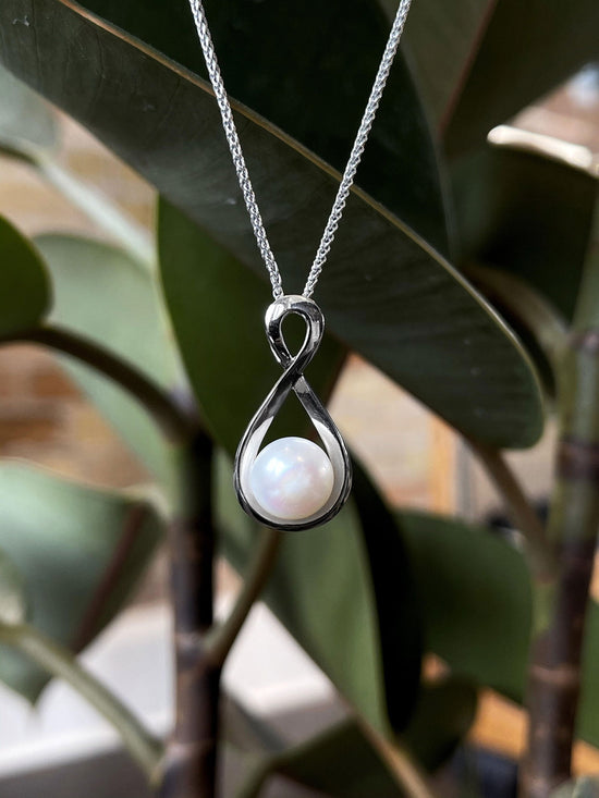 Photo of Pearl Infinity Necklace in a decorative scene, designed by , available at Plumb Gold & Plumb Silver