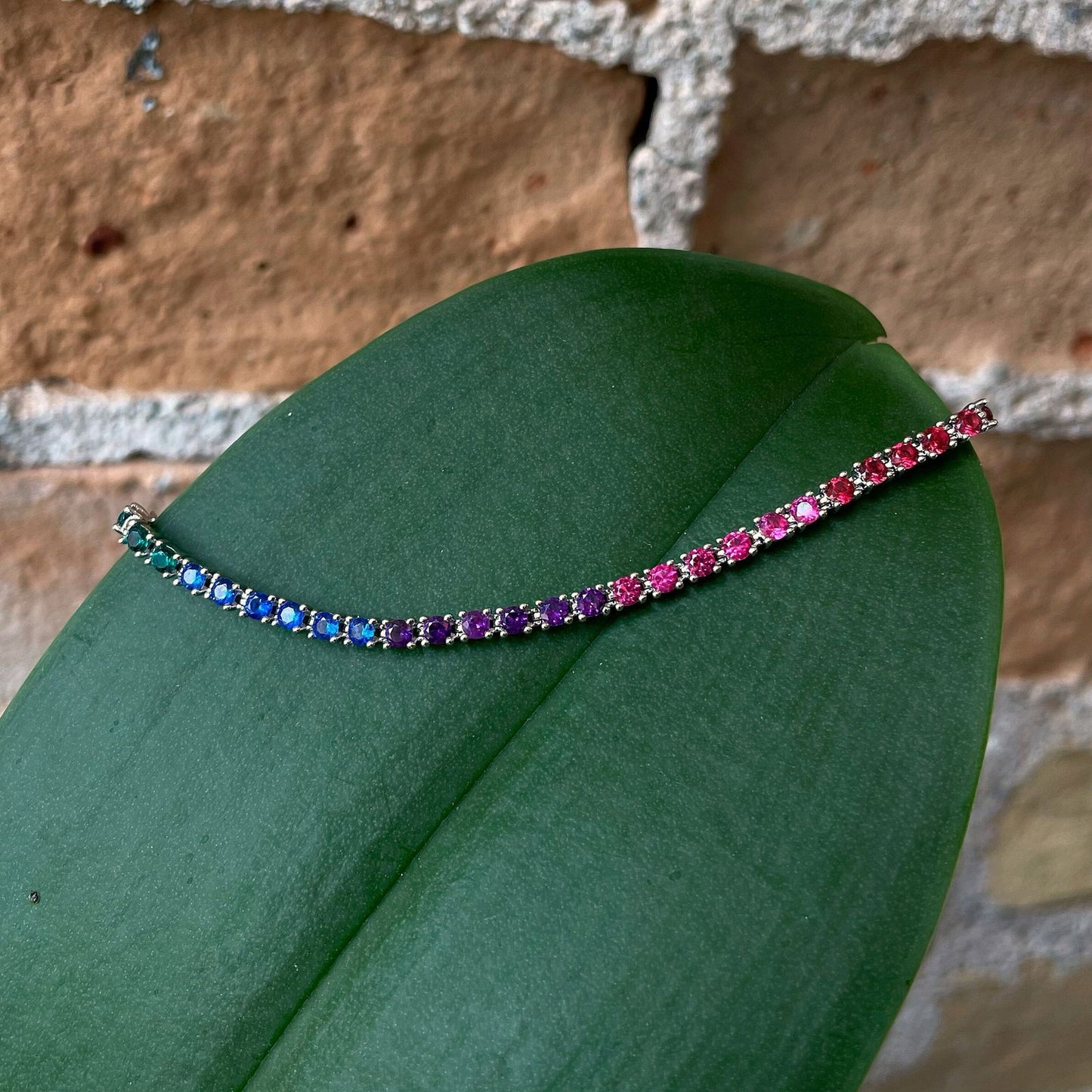 Photo of Rainbow Tennis Bracelet in a decorative scene, designed by , available at Plumb Gold & Plumb Silver