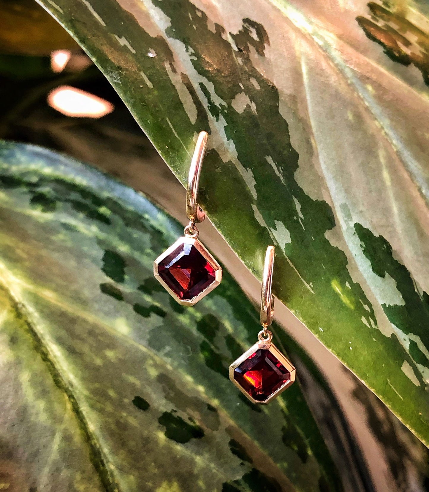 Photo of Red Garnet Huggie Dangle Gold Earrings in a decorative scene, designed by , available at Plumb Gold & Plumb Silver