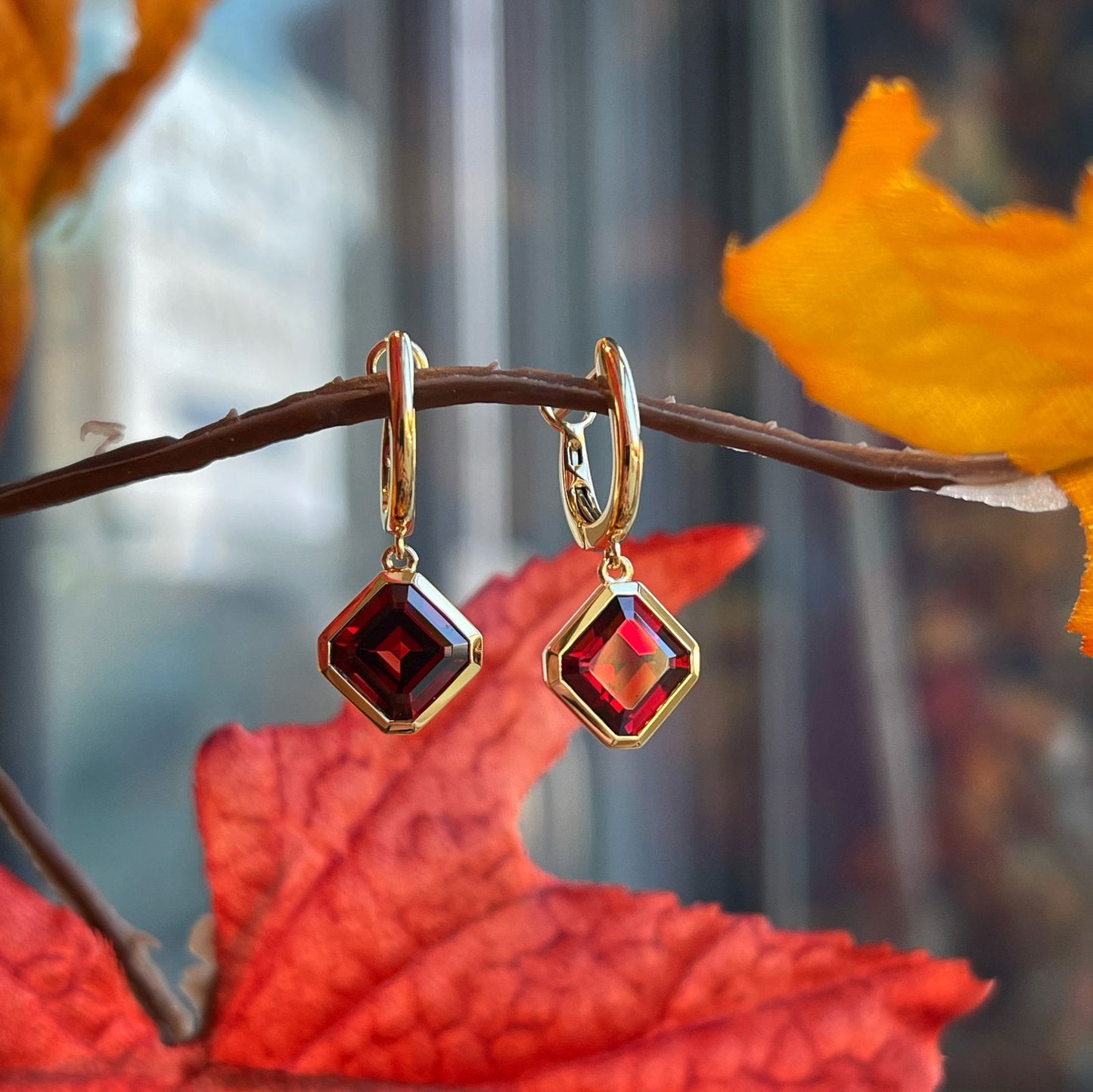 Photo of Red Garnet Huggie Dangle Gold Earrings in a decorative scene, designed by , available at Plumb Gold & Plumb Silver