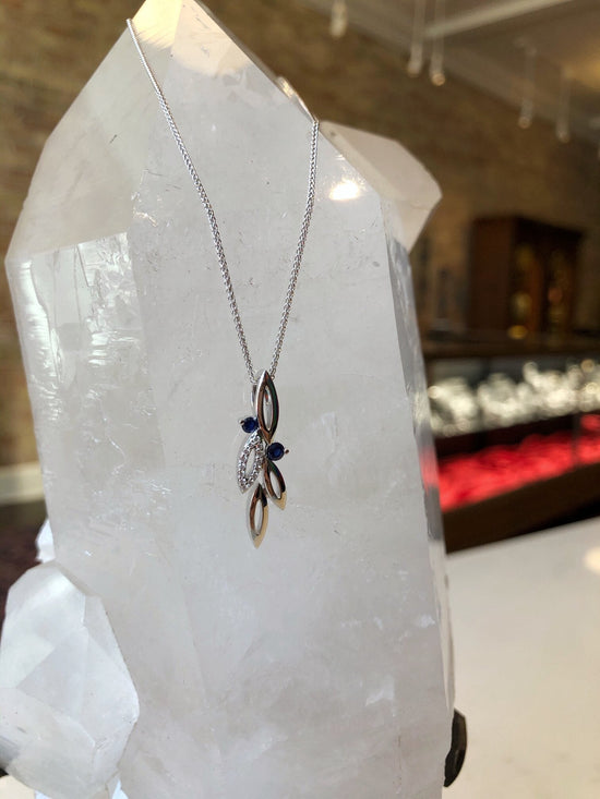 Photo of Sapphire and Diamond Flora Pendant in a decorative scene, designed by , available at Plumb Gold & Plumb Silver