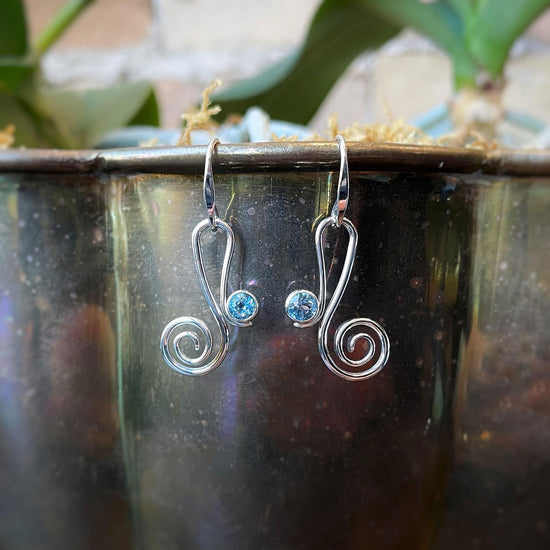 Photo of "Script" Blue Topaz Earrings in a decorative scene, designed by , available at Plumb Gold & Plumb Silver