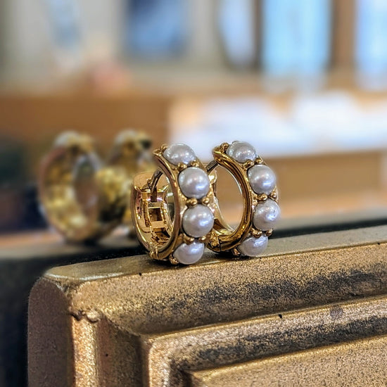 Photo of Simulated Pearl Huggies Earrings in a decorative scene, designed by , available at Plumb Gold & Plumb Silver