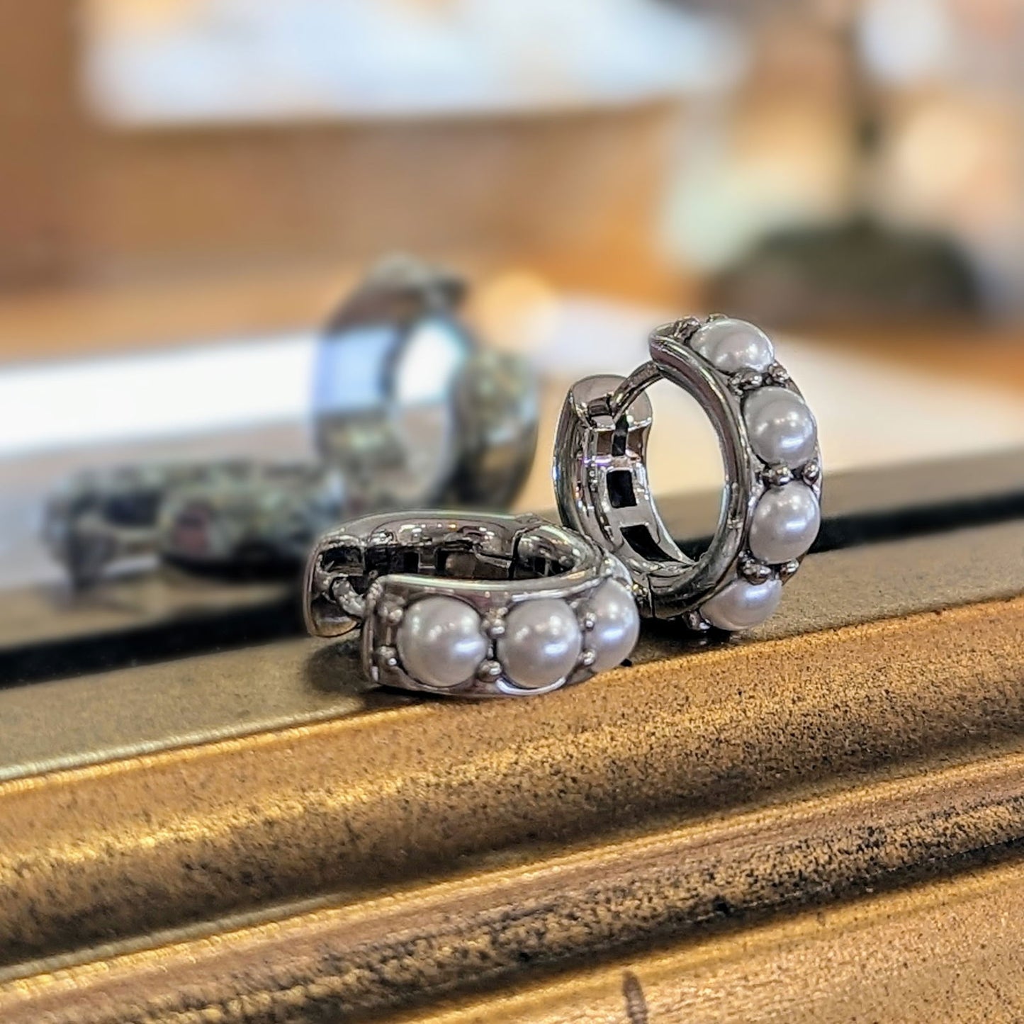 Photo of Simulated Pearl Huggies Earrings in a decorative scene, designed by , available at Plumb Gold & Plumb Silver