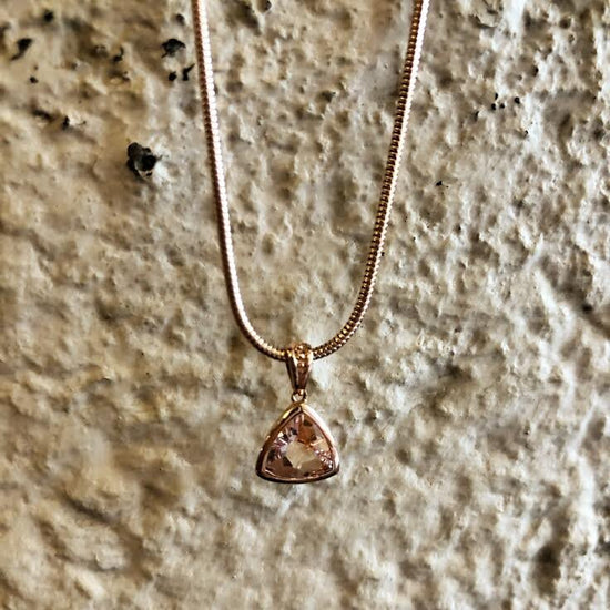 Photo of Stanton Color Trillion Morganite Bezel Pendant in a decorative scene, designed by , available at Plumb Gold & Plumb Silver