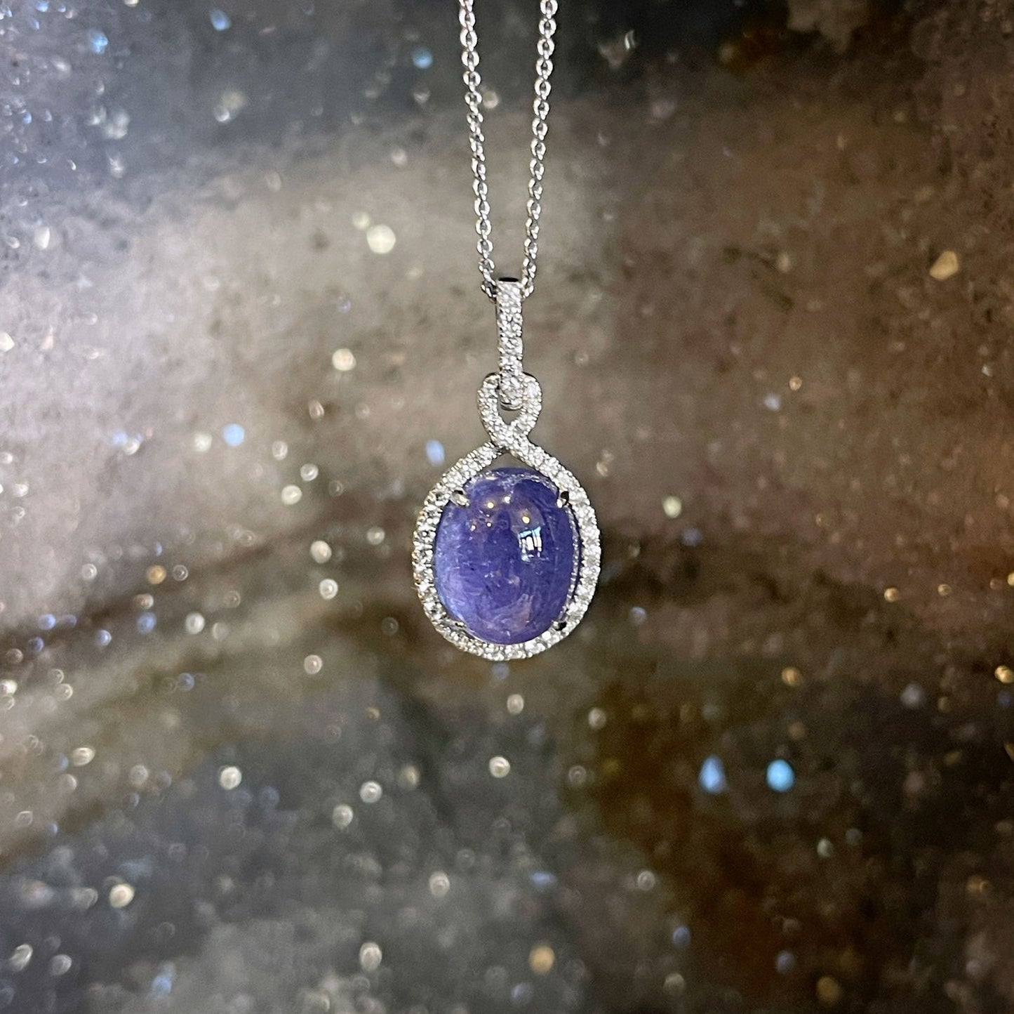 Photo of Tanzanite Cabochon and Diamond Necklace in a decorative scene, designed by , available at Plumb Gold & Plumb Silver