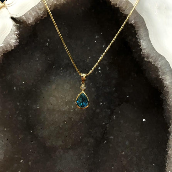 Photo of Teardrop Blue Zircon Pendant in a decorative scene, designed by , available at Plumb Gold & Plumb Silver