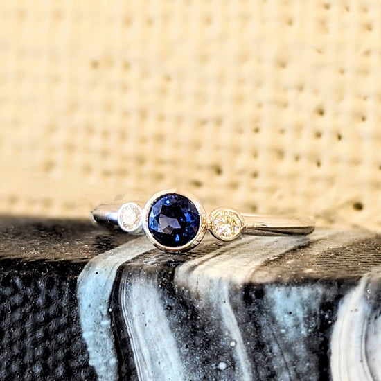 Photo of Three Stone Bezel Ring in a decorative scene, designed by , available at Plumb Gold & Plumb Silver